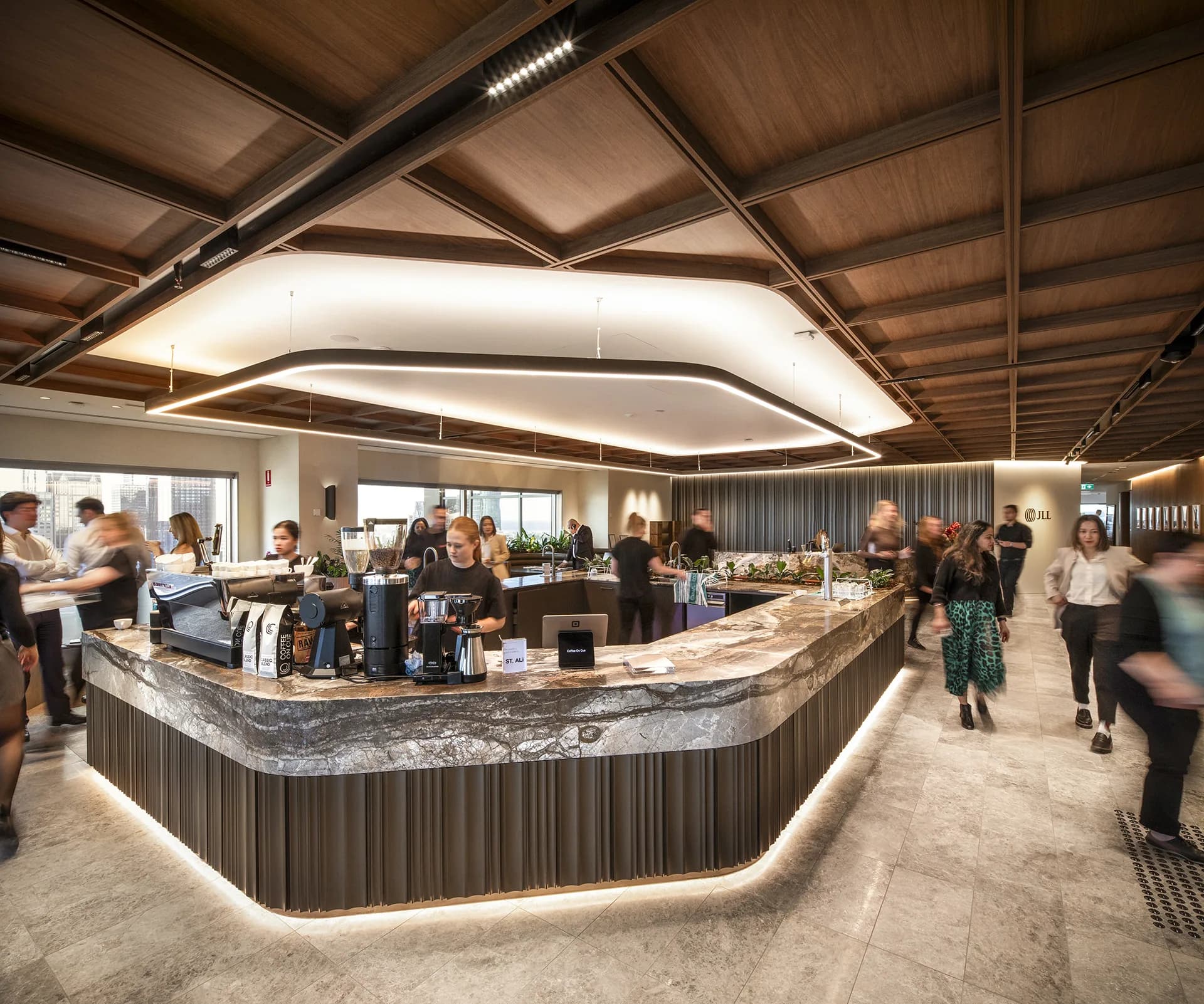 The Coffee on Cue in-house barista bar at JLL, 101 Collins Street, Melbourne: a barista at the marble espresso counter as staff move through, the city skyline through the windows