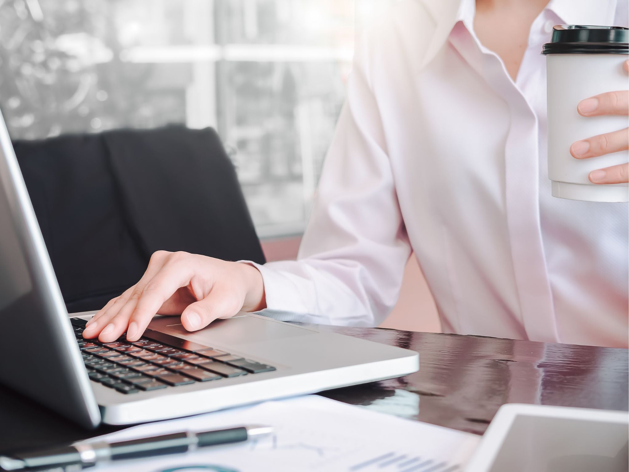 Employee working on laptop with coffee in hand